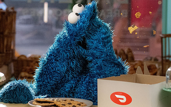 A blue furry monster eats chocolate chip cookies from a white cardboard box.