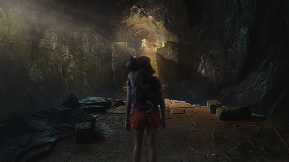 A person with a small animal on their back stands in a dark cave looking toward a bright opening.