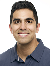A smiling man with short dark hair wearing a dark blue collared shirt.