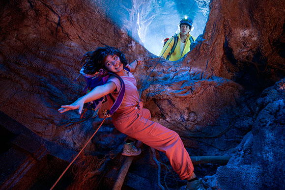 A person in pink jumps through a cave while another person in yellow watches from above.