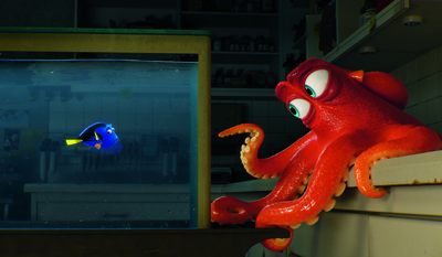 A large red octopus leans over a counter, staring at a small blue tang fish inside a rectangular glass tank.