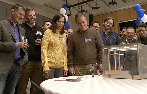 A group of people smiling and looking down at a small architectural model on a white table.
