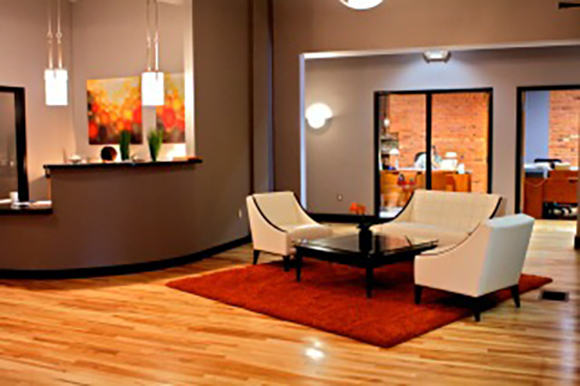 A modern lounge with white armchairs, a white sofa, a dark coffee table, and a red rug on hardwood floors.