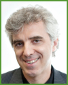 A smiling man with wavy grey hair wearing a dark blazer over a black shirt.
