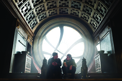 Two people sit in silhouette before a large, bright circular window in a grand, coffered hall.