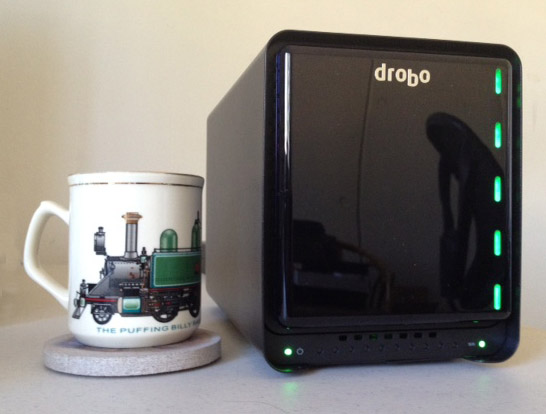 A white mug featuring a steam engine illustration sits beside a black Drobo storage device.