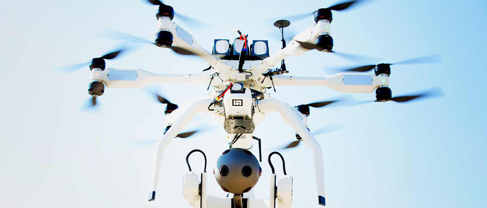 A white multi-rotor drone with multiple propellers flying against a bright blue sky.