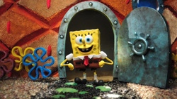 A claymation SpongeBob SquarePants stands in a rounded doorway of a textured orange structure.