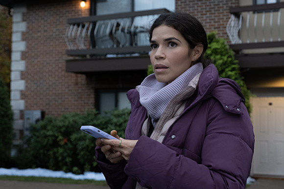 A woman in a purple puffer jacket and white turtleneck holds a smartphone outdoors.