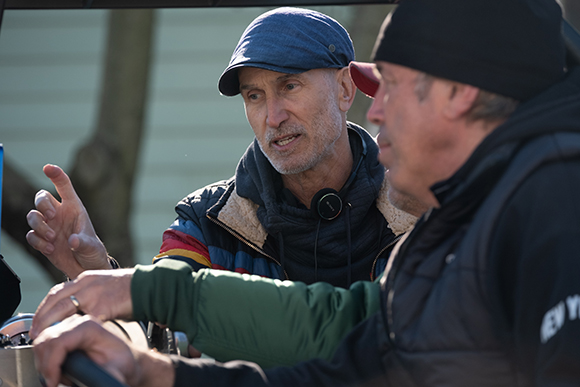 A man in a blue cap and jacket talks to another man in a black beanie and jacket.