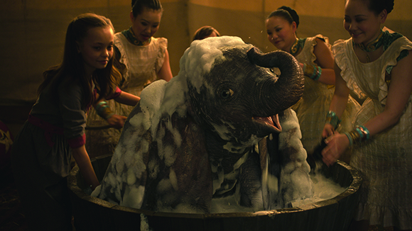 Four young women surround a large wooden tub, bathing a small elephant covered in white soap suds.