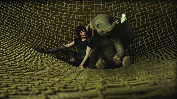 A woman in black clothing sits beside a large plush elephant inside a large rope net.