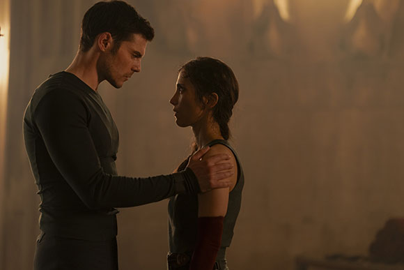 A man in a dark long-sleeve shirt places his hands on a woman's shoulders as they look at each other.