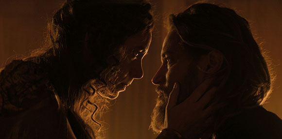 Two men in profile facing each other closely in warm, dim light.