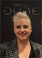 A woman with short blonde hair smiling in front of a black Dune HBO Original backdrop.