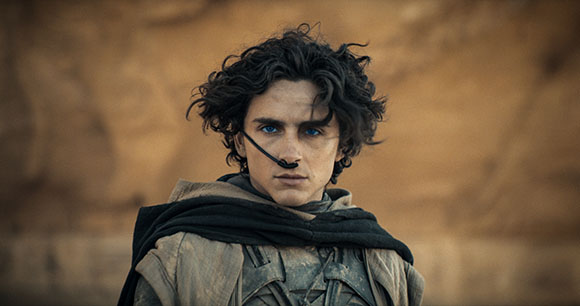 A young man with dark curly hair wearing a dark cloak and a thin breathing tube under his nose.