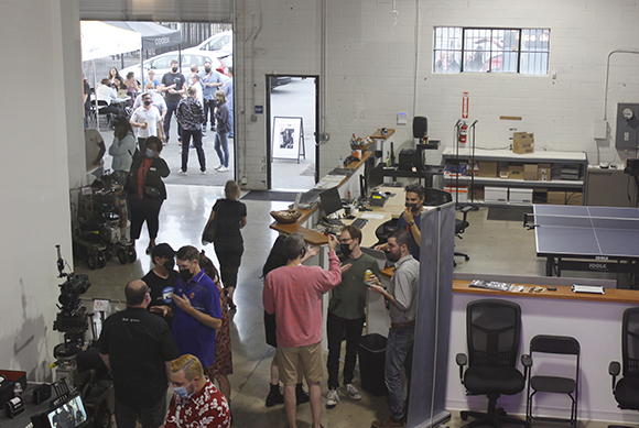 People standing and talking in a large, open room with high ceilings and an open doorway.