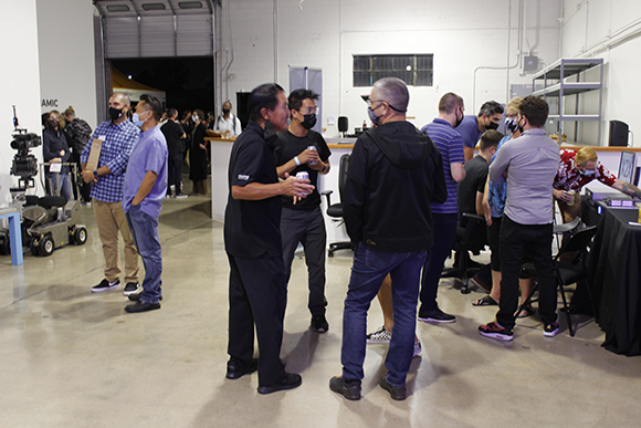 A group of people standing and talking in a large, brightly lit industrial warehouse or studio space.