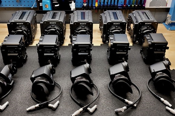 Five rows of black Sony professional video cameras and equipment laid out on a workbench.