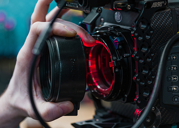 Hands adjusting a large professional camera lens with red light reflecting inside the mount.