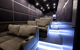Luxury mobile lounge interior with plush grey sofas and blue LED floor lighting.