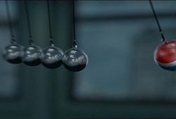 Four silver metal spheres hanging in a row next to a single red sphere in a Newton's cradle.