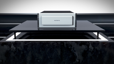 A white rectangular electronic device with the word ELEMENTS on it sits on a black platform.