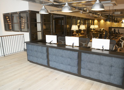 A long, dark wood reception desk with blue tufted fabric panels in a modern open-plan office.