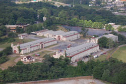 Aerial view of several long, white industrial buildings surrounded by green trees and parking lots.