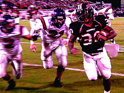 Football players in white and black uniforms running on a grass field under stadium lights.
