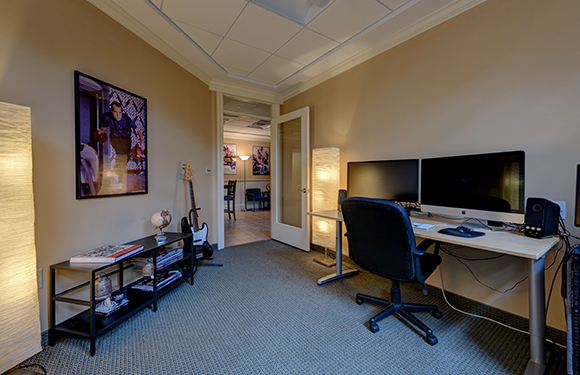 A home office featuring a desk with dual monitors, a black office chair, and a bookshelf.