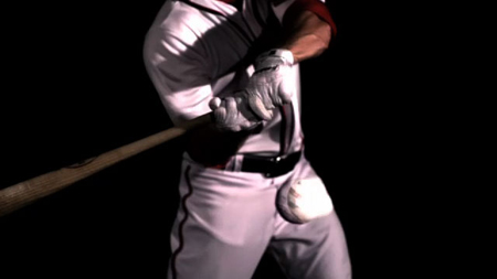 A baseball player in a white uniform swings a wooden bat against a black background.