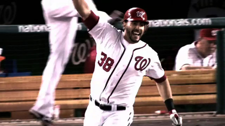A baseball player in a white Washington Nationals uniform celebrates with arms raised.