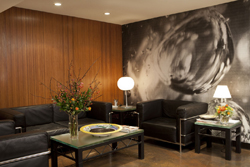 Black leather sofas and armchairs arranged in a room with wood paneling and a large black and white mural.