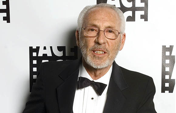 An older man with gray hair and a beard wearing glasses and a black tuxedo with a bowtie.