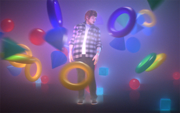 A man in a checkered shirt stands surrounded by floating, glowing rings and geometric shapes in purple light.