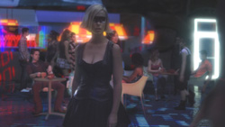 A blonde woman in a black dress stands in a dark, crowded nightclub with neon lights.