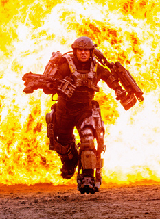 A soldier in dark mechanical exoskeleton armor runs toward the camera against a backdrop of large orange flames.