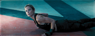 A woman in black athletic gear performs a push-up on a red mat in a dimly lit setting.