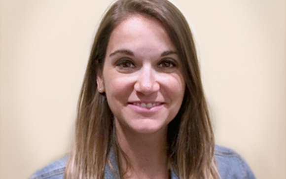 A smiling woman with long brown hair looking directly at the camera against a plain beige background.