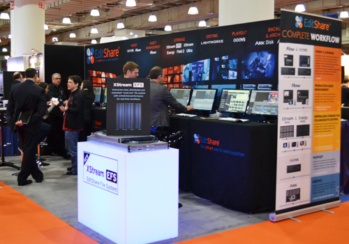 People standing at an EditShare trade show booth featuring large displays and product information banners.