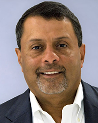 A man with short dark hair and a grey-flecked goatee wearing a white shirt and dark blazer.