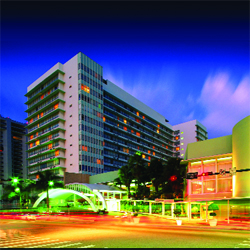 A tall, white multi-story building with lit windows under a deep blue twilight sky.