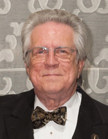 Close-up of a man with graying hair and glasses wearing a tuxedo and a patterned bow tie.