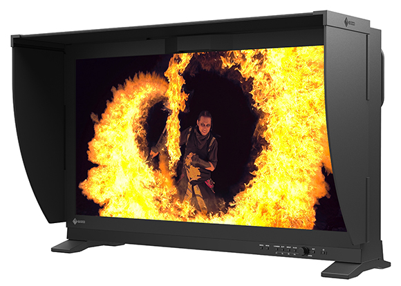 A large black professional monitor displaying a cinematic scene of a person surrounded by swirling flames.