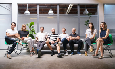 Eight people sitting on chairs and a sofa in a bright, modern office space.
