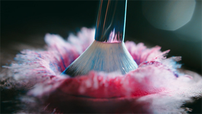 A makeup brush dipping into a cloud of vibrant pink and blue cosmetic powder.