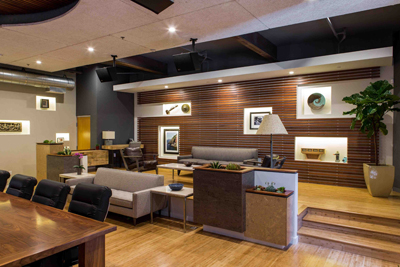 A modern lounge with wooden slat walls, gray sofas, a large potted plant, and a wooden table.