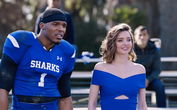 A football player in a blue Sharks jersey looks toward a woman in a blue off-the-shoulder dress.