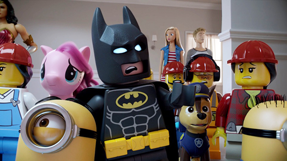 LEGO Batman stands centrally among a pink pony, Minions, and other toy characters in a room.